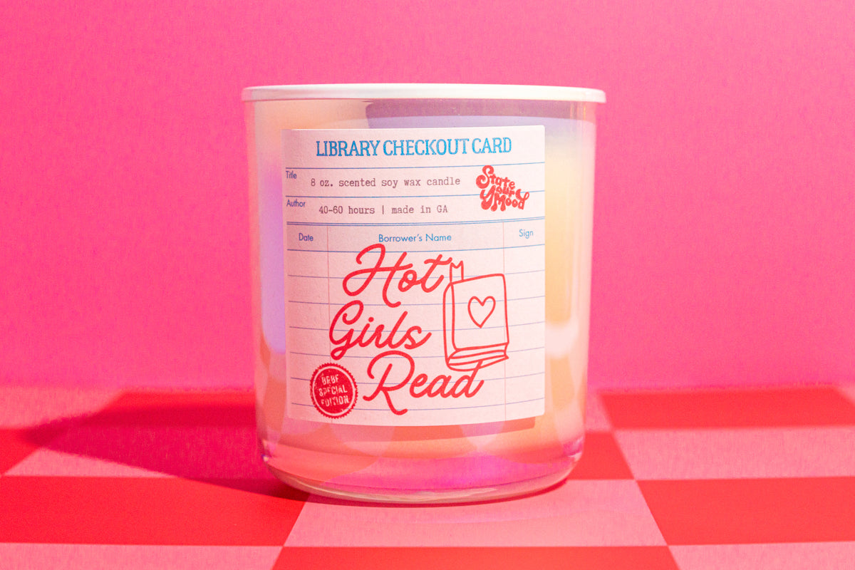 Candle with a label resembling a library checkout card on a pink and red checkered surface