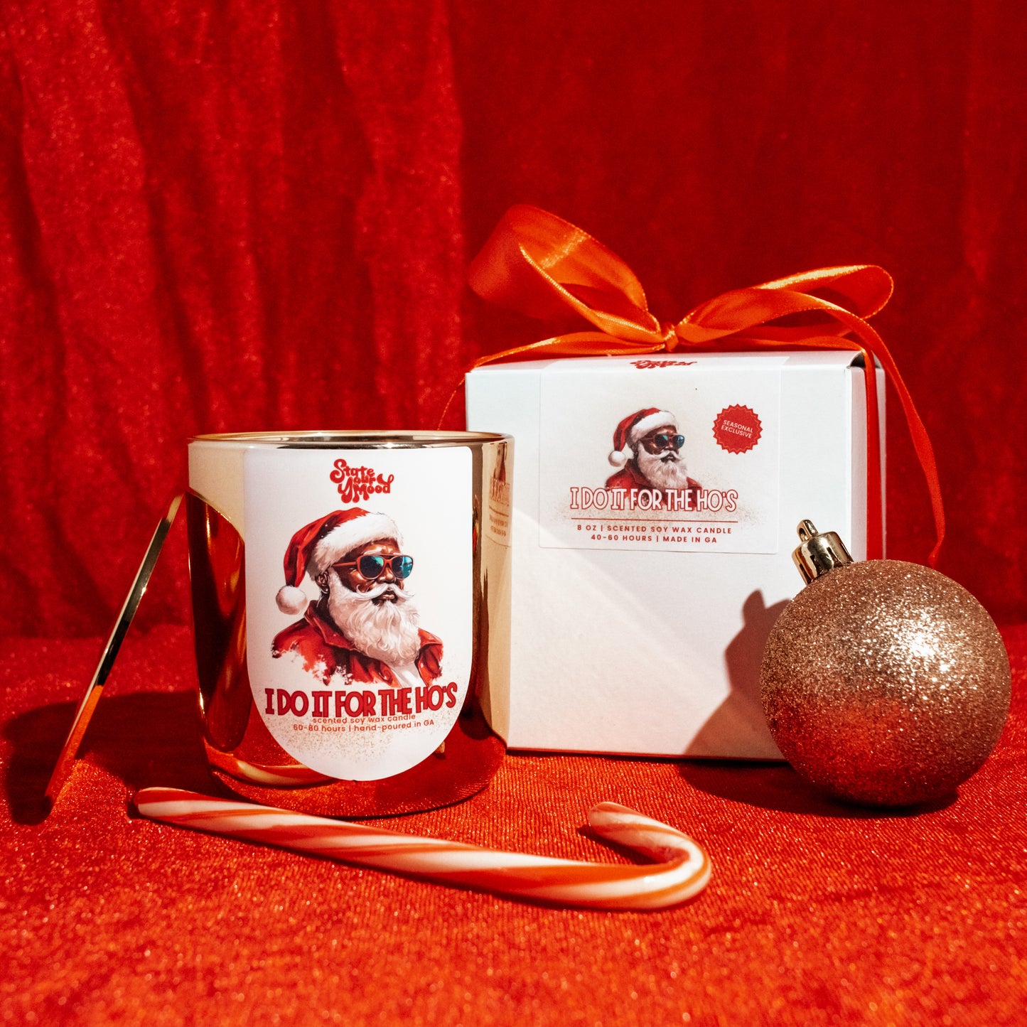 gold jar candle with santa label, candy cane, and gift box on red velvet